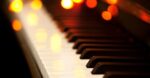 Close-up of piano keys with warm, out-of-focus holiday lights creating a cozy winter atmosphere.