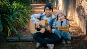 children smiling with guitar outside