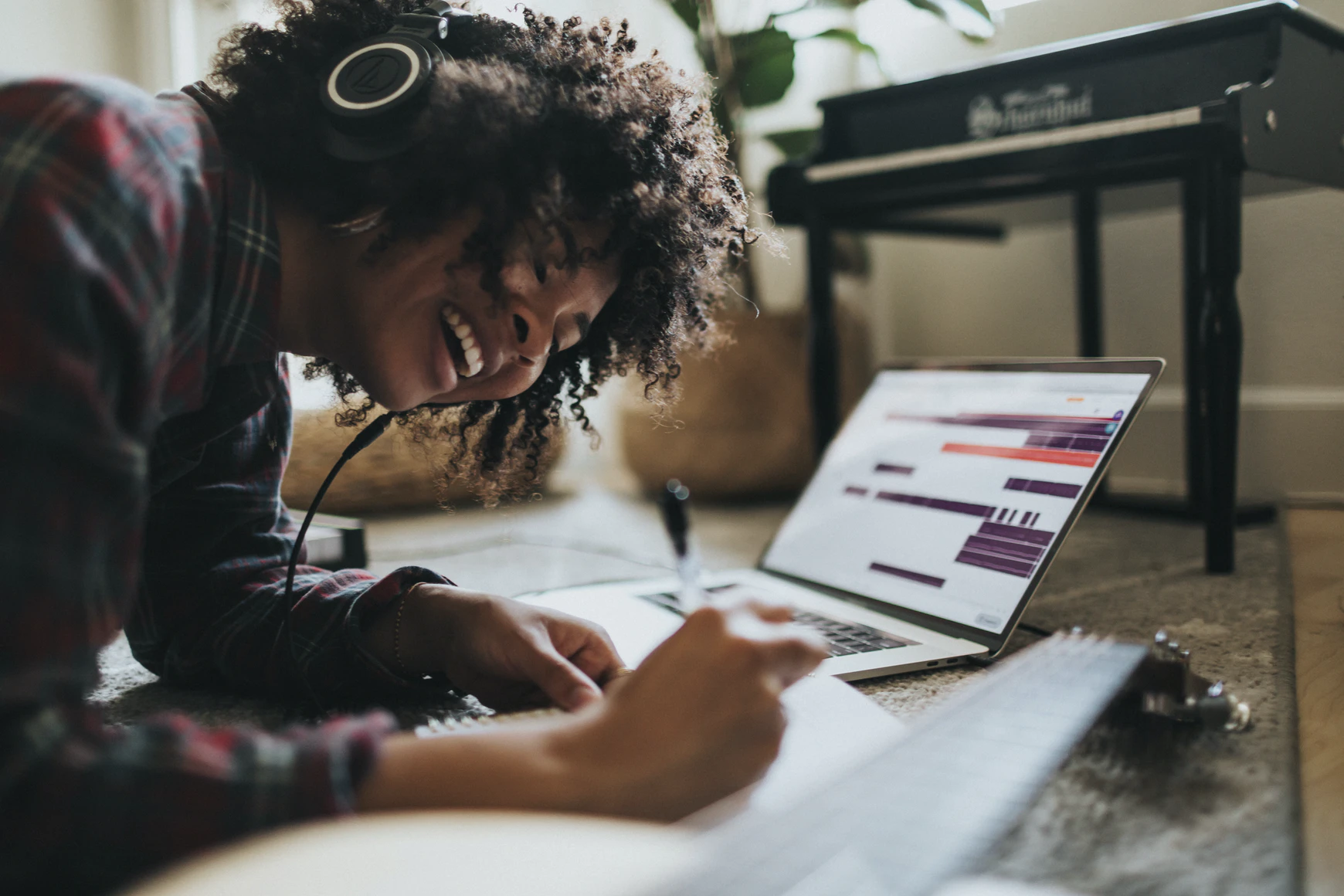 young lady smiling, writing, listening to music with computer in the background