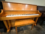 Used Boston UP-118 upright piano in oak finish with matching bench, displayed in a showroom setting.