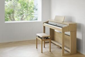 Light-wood Roland digital piano and matching bench in a bright, minimalist room with a large window.